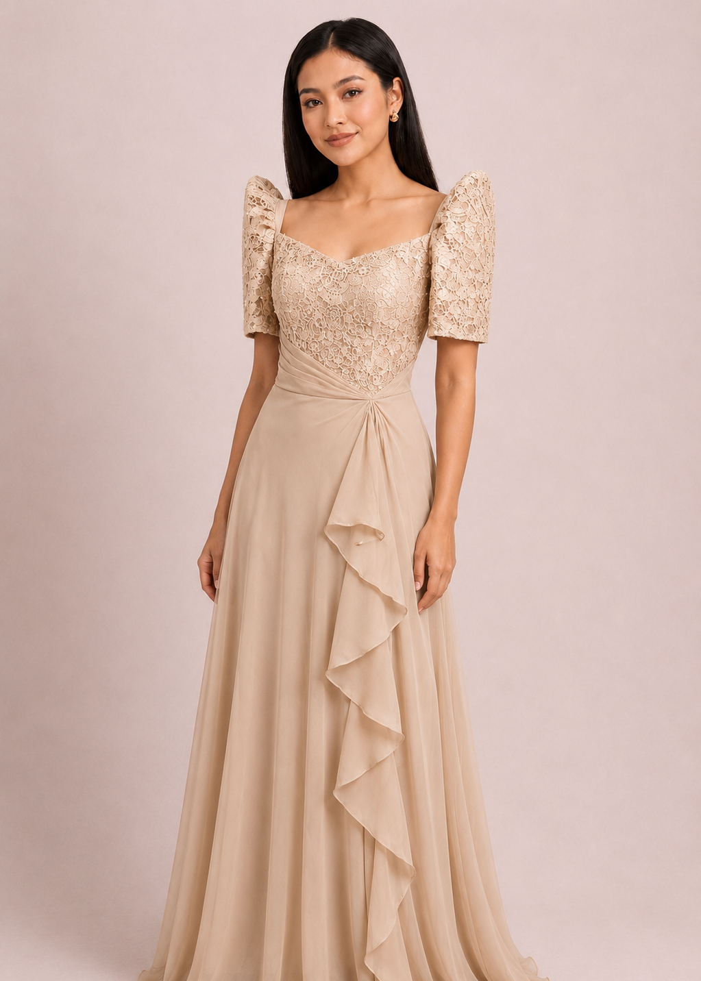 Corazon filipiniana dress in cream pleated chiffon - A woman modeling a floor-length champagne beige gown with a lace bodice, puff sleeves, and a layered ruffle skirt, set against a solid light beige studio background.
